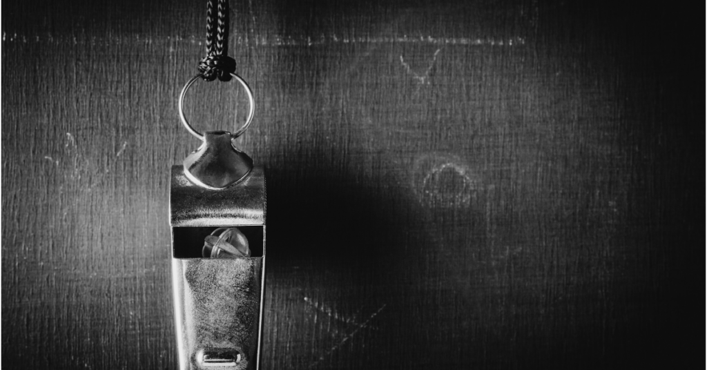 now this one Close-up of a metal whistle hanging from a cord against a dark textured background, with light highlighting its surface.